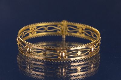 gros plan d'un bracelet en or sur une surface noire