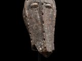 un masque en bois posé sur un socle, sur fond noir