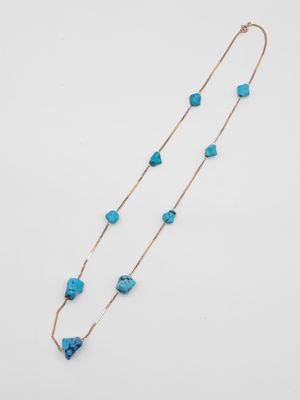 un long collier composé de perles de turquoise et d'une chaîne en or