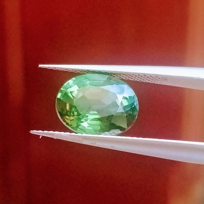 un gros plan d'une pierre précieuse verte tenue par une paire de pinces