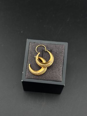 une paire de boucles d'oreilles en or dans un écrin noir posé sur une surface noire