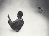 photographie en noir et blanc d'une femme assise par terre, tenant un papillon dans la main