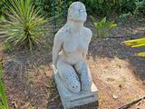 une statue représentant une femme assise sur un bloc de pierre au milieu d'un jardin