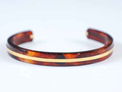 un bracelet en écaille de tortue avec des rayures dorées sur fond blanc