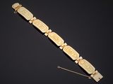 un bracelet en or orné de visages sculptés et d'une chaîne sur fond noir