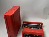 une machine à écrire rouge à côté d'une boîte rouge posée sur une surface blanche