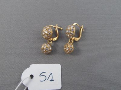 une paire de boucles d'oreilles dorées et une étiquette de prix posée sur une surface grise