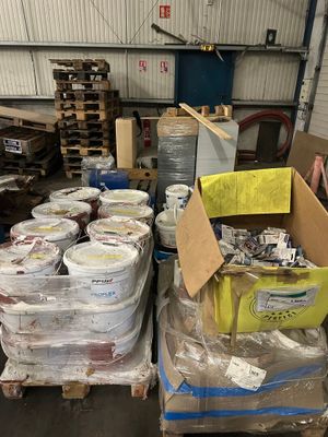de nombreux seaux de peinture posés sur des palettes dans un entrepôt