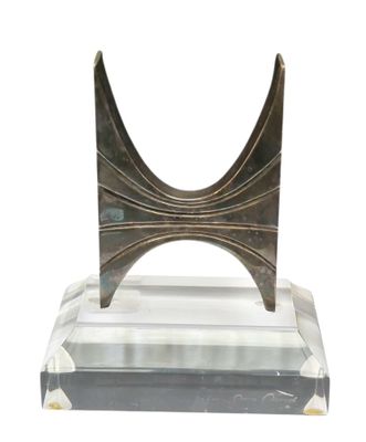 une sculpture en métal posée sur un socle transparent, sur fond blanc