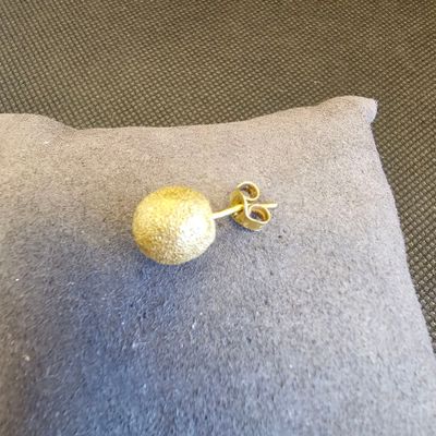 des boucles d'oreilles à clous en forme de boule dorée posées sur un coussin, sur un sol recouvert de moquette