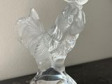 une figurine en verre transparent représentant un coq, posée sur une table
