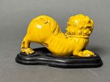 chinese carved figurine of a yellow lion on a black base