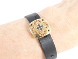 someone is wearing a black leather bracelet with gold and blue stones