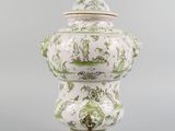 a white and green vase with a lid on a stand