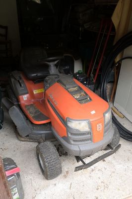 une tondeuse autoportée orange garée dans un garage, à côté d'un tas d'outils