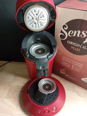 une cafetière rouge posée sur une table à côté d'une boîte