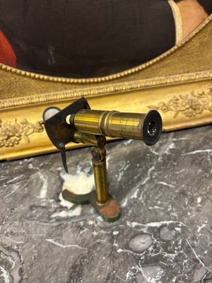 un télescope doré posé sur une table en marbre, à côté d'un miroir