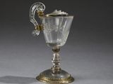 une coupe ancienne en argent et en verre, munie d'une anse, posée sur une surface grise