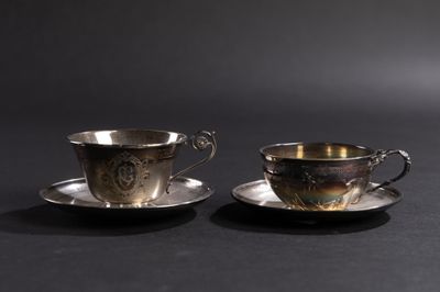 deux tasses et soucoupes en argent posées sur un fond noir