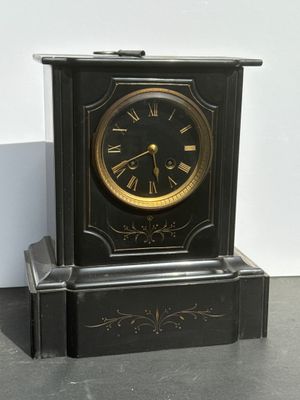 a black clock sitting on the floor in front of a white wall