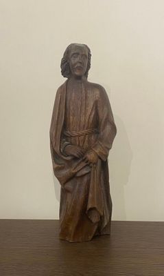 statue d'un homme assis sur une table en bois, avec un mur blanc en arrière-plan
