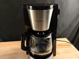 a coffee maker on a wooden table with a black wall behind it