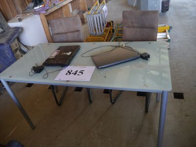 une table sur laquelle est posé un ordinateur portable, avec une chaise à l'arrière-plan