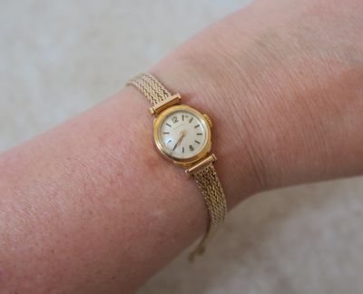 le poignet d'une femme auquel est accrochée une montre en or