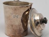 an old silver cup with a lid sitting on a white surface