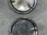 two silver plates sitting on a table with a black background