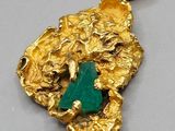 a close up of a gold pendant with a green stone