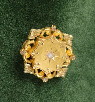 une photo d'une broche en or et diamants posée sur un tissu vert