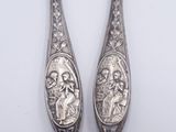 pair of silver spoons with religious images on them on a white surface