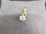 pendentif en or jaune serti d'un diamant, posé sur un coussin, sur fond gris