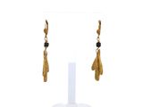 une paire de boucles d'oreilles en or ornées de perles noires sur un support blanc