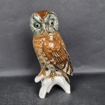 a ceramic owl sitting on a branch on a gray background