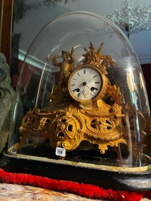 une horloge en or posée sur une table, sous une cloche en verre