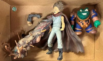 deux figurines dans une boîte : l'une représente un homme avec une cape et l'autre un monstre