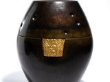 un vase noir avec un couvercle doré posé sur une surface blanche