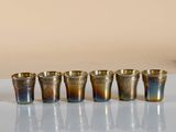 six glasses sitting on a table with a vase in front of them