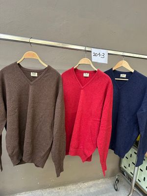 trois pulls suspendus à un portant dans un magasin, avec une étiquette de prix