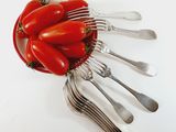 tomatoes in a bowl with forks and spoons on a white surface