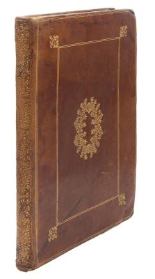 un vieux livre marron avec des bordures dorées posé sur une surface blanche