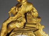 a gold clock with a woman sitting on top of it