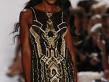 the woman is walking down the runway in a black and gold dress