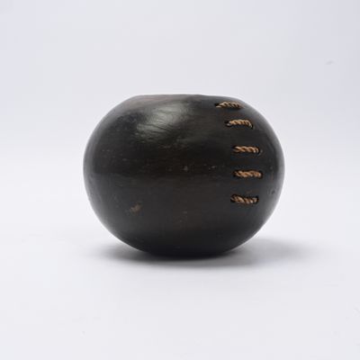 une boule noire percée de trous, posée sur une surface blanche