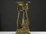un vase doré posé sur une table blanche, sur fond noir