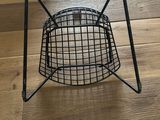a black wire basket on a wooden floor with a plant in it