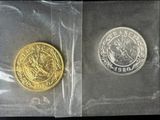 two gold and silver coins in plastic bags on a black surface
