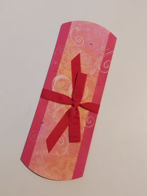 boîte-cadeau rose et orange ornée d'un ruban rouge sur un fond blanc